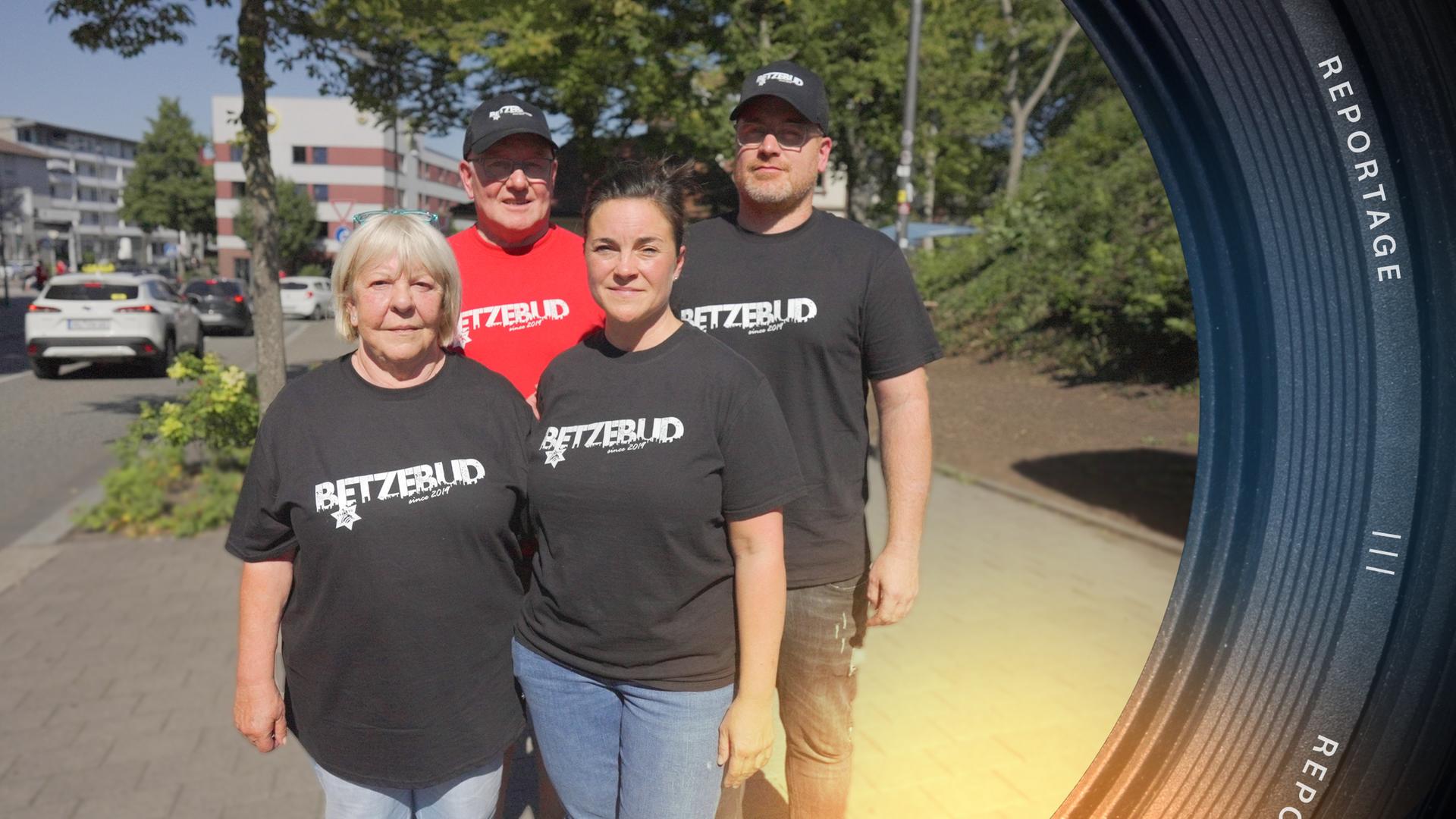 Helga Reitmayer, Armin Kraus, Sandy Kraus, Armin Kraus jr. stehen eng beieinander. Die zwei Männer tragen Mützen. Alle vier tragen T-Shirts mit der Aufschrift "Betzebud".
