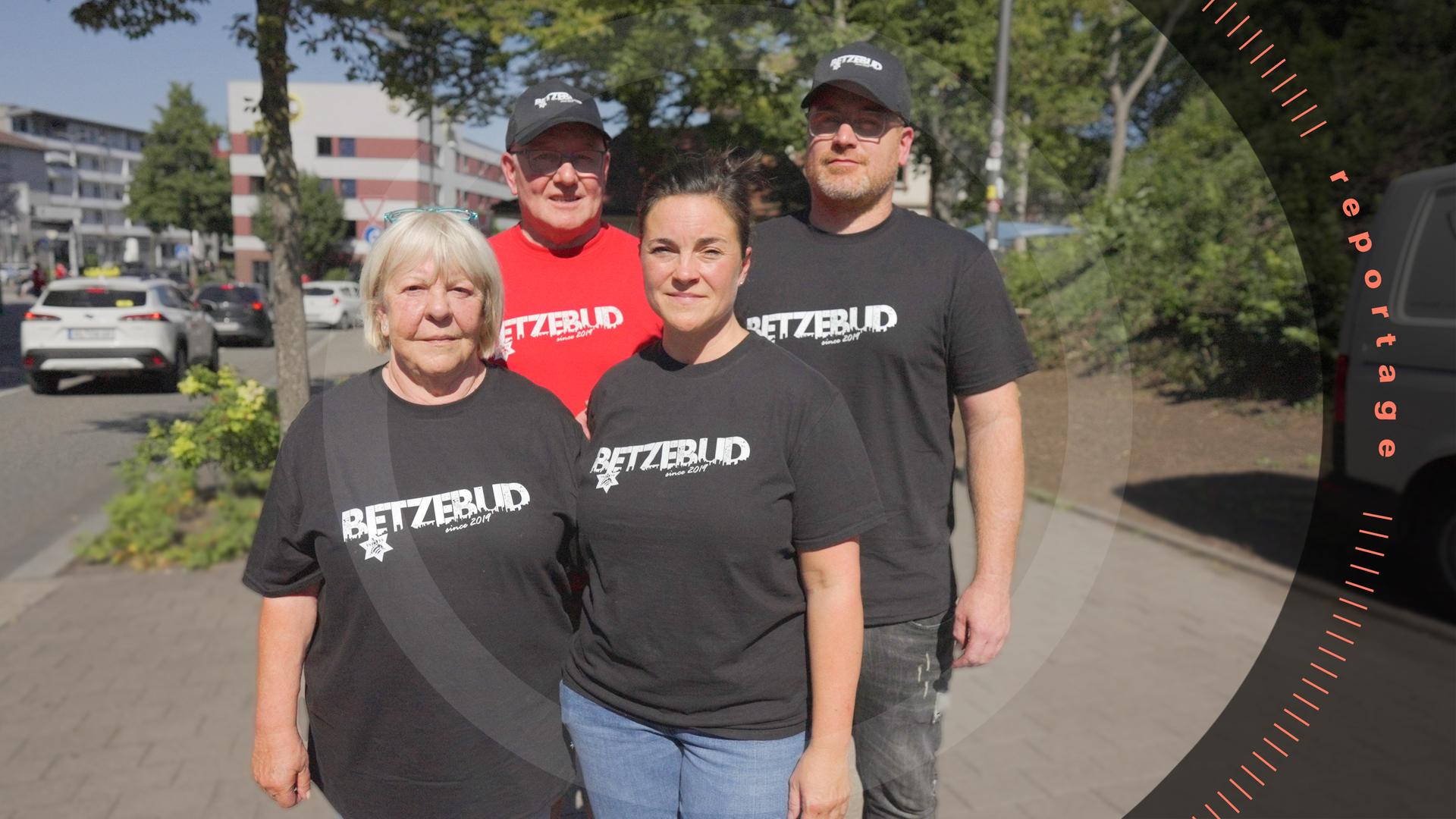 Helga Reitmayer, Armin Kraus, Sandy Kraus, Armin Kraus jr. stehen eng beieinander. Die zwei Männer tragen Mützen. Alle vier tragen T-Shirts mit der Aufschrift "Betzebud".