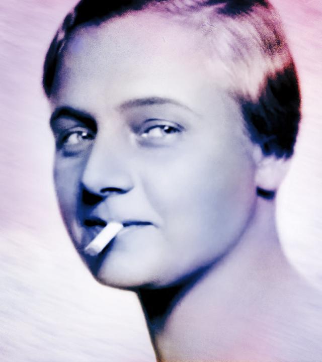 Das Bild zeigt eine schwarz-weiße Fotografie einer Frau, die mit einem selbstbewussten Ausdruck in die Kamera blickt. Sie hat kurzes, glattes Haar, das zur Seite gestylt ist. Zwischen ihren Lippen hält sie eine Zigarette. Der Hintergrund ist hell und unscharf, wodurch der Fokus auf ihrem Gesicht liegt. Die Frau hat eine leichte Lächeln, das eine gewisse Nonchalance ausstrahlt. Die Beschreibung bezieht sich auf die Person im Kontext des Films „Kampf der Frauen – Anfänge der Frauenbewegung in Österreich“, der sich mit der Geschichte der Frauenbewegung zur Jahrhundertwende beschäftigt.