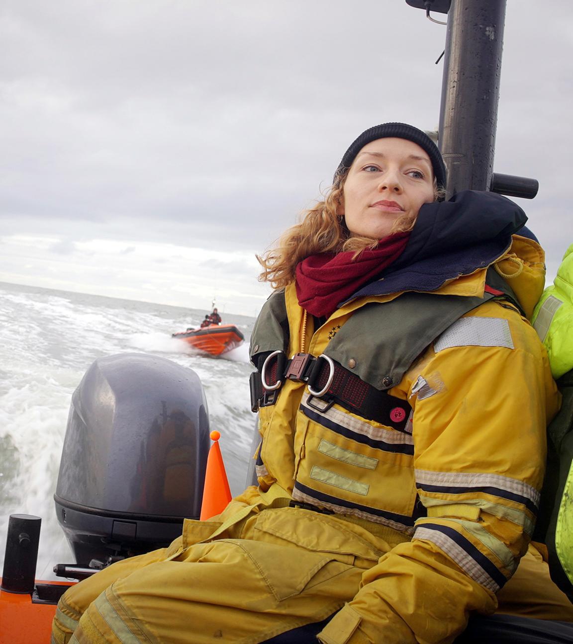 Franziska Saalmann von Greenpeace in gelbem Overall und olivgrüner Schwimmweste fährt im Schlauchboot auf grauer See. Im Hintergrund sieht man ein rotes Boot mit 2 Personen.
