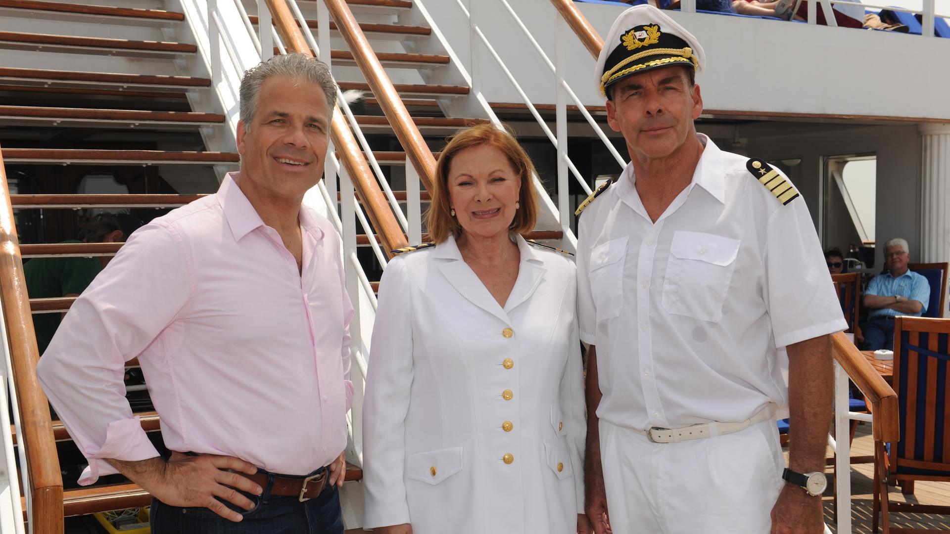 "Das Traumschiff: Kanada": Zusammen mit Peter Rand (Karsten Speck) und Beatrice (Heide Keller) steht Kapitän Burger (Sascha Hehn) an Deck des Schiffs. Sie lächeln in die Kamera.