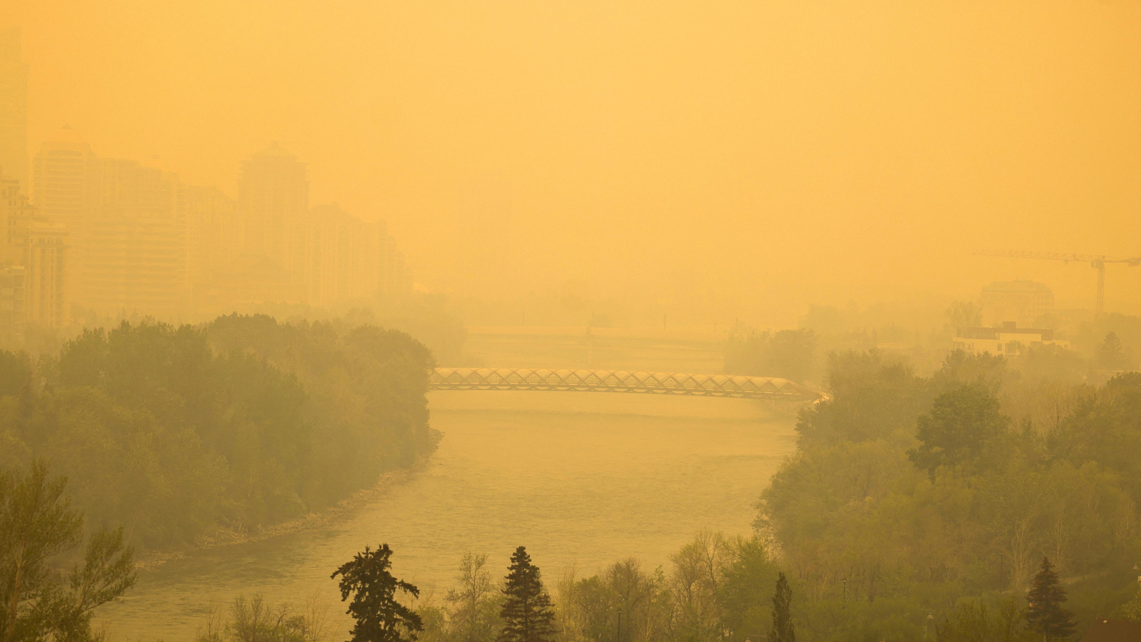 Orangener Rauch über einem Wald-, Fluß- und Stadtgebiet in Folge von Waldbränden.