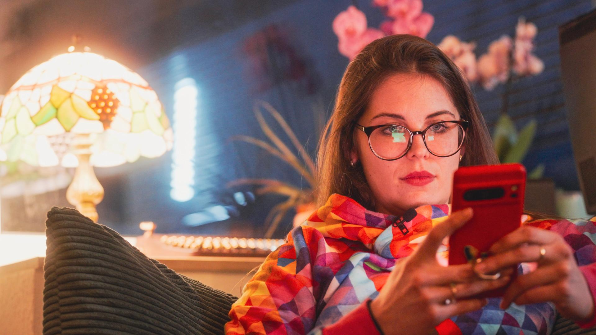 Alice sitzt zuhause auf dem Sofa und chattet mit einer KI. Neben ihr leuchtet eine Lampe.