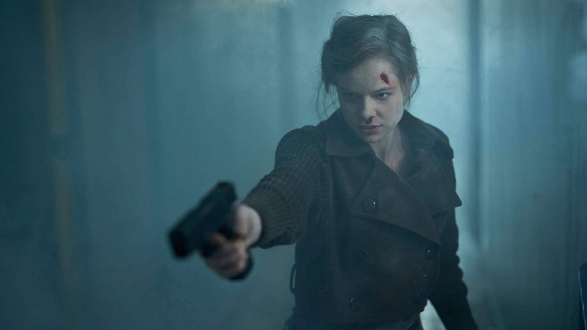 "Westwall - Kapitel II": Julia (Emma Bading) steht nach einer Explosion mit einer Pistole in der Hand im verrauchten Treppenhaus von Nicks Wohnhaus.