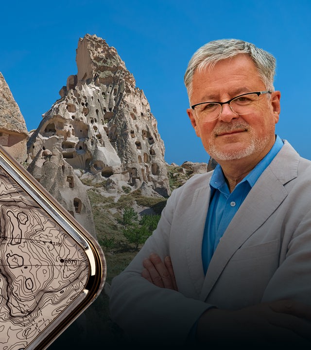 Christopher Clark vor blauem Himmel und Felsen, die Löcher haben. Sie dienen den Menschen seit Jahrhunderten als Behausung.