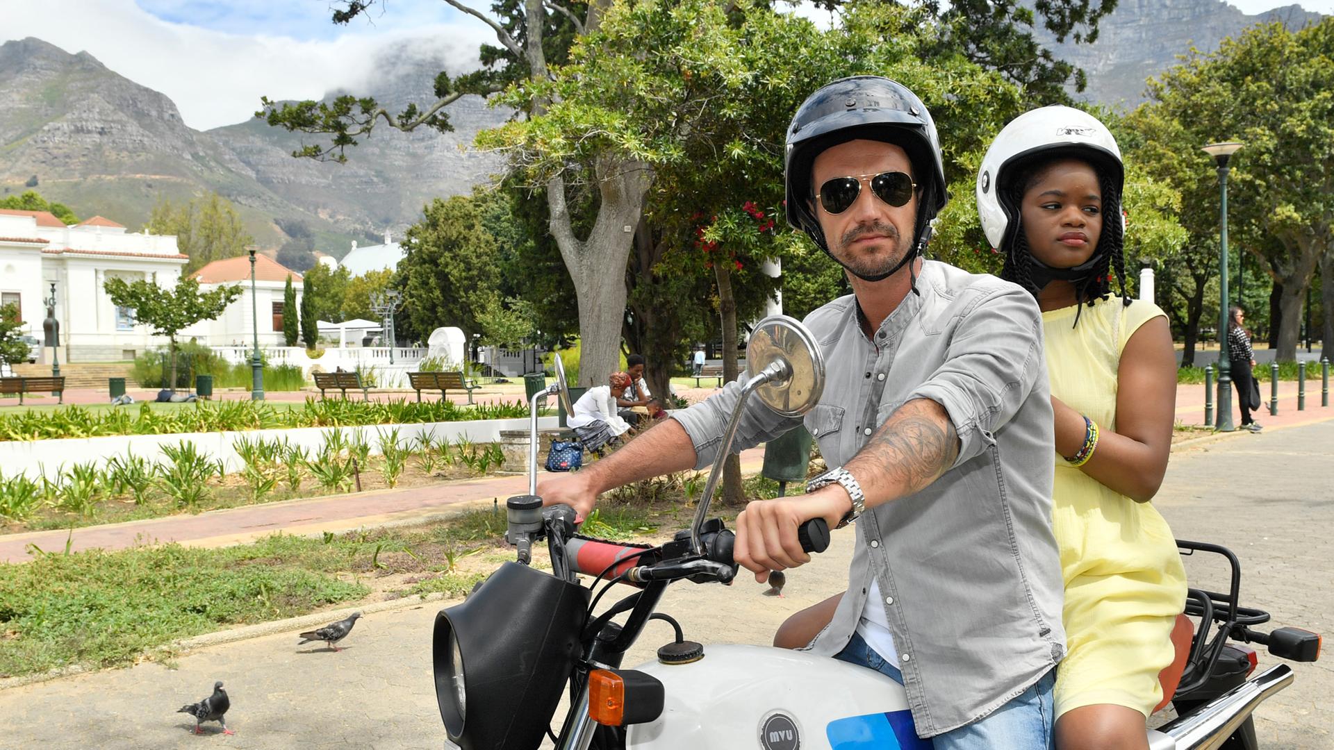 Kapitän Max Parger (Florian Silbereisen) und Lea Bremer (Melodie Wakivuamina) sitzen zusammen auf einem Motorrad.