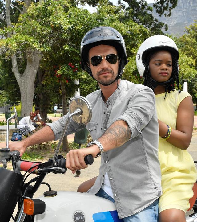 Kapitän Max Parger (Florian Silbereisen) und Lea Bremer (Melodie Wakivuamina) sitzen zusammen auf einem Motorrad.