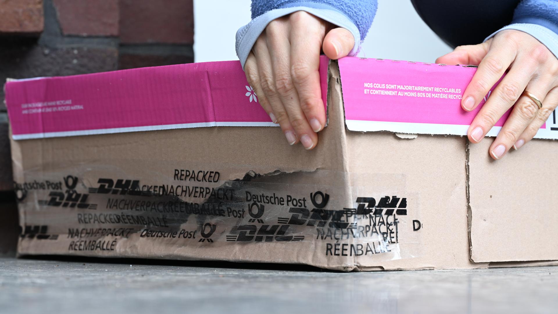 Eine Frau nimmt ein kaputtes Paket hoch, das vor ihrer Haustür liegt.