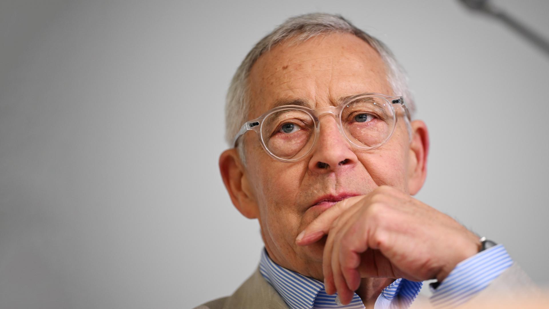 Porträtfoto eines älteren Mannes mit Brille, der nachdenklich eine Hand an den Mund legt.