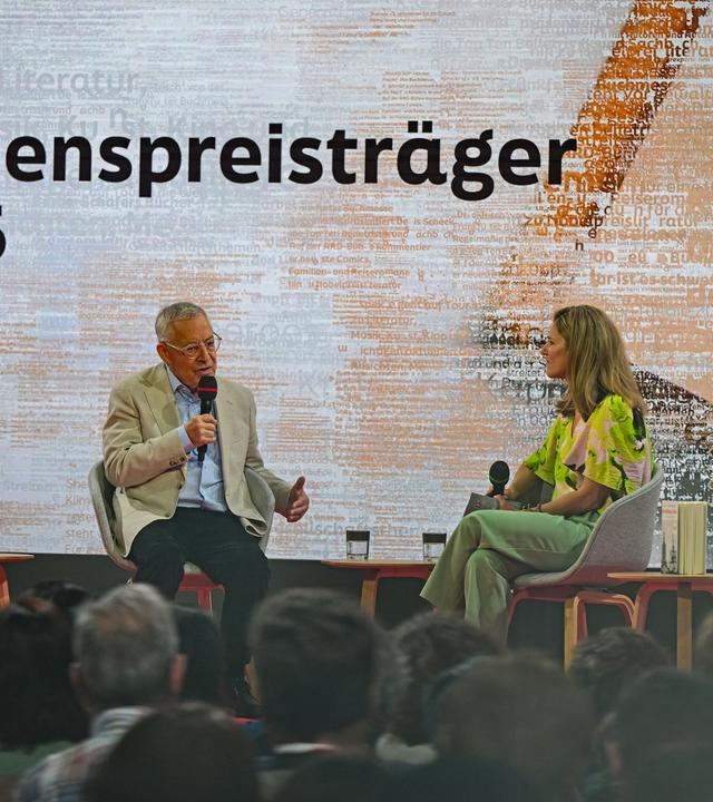 Eine Frau und ein Mann sitzen auf einer Bühne und diskutieren.