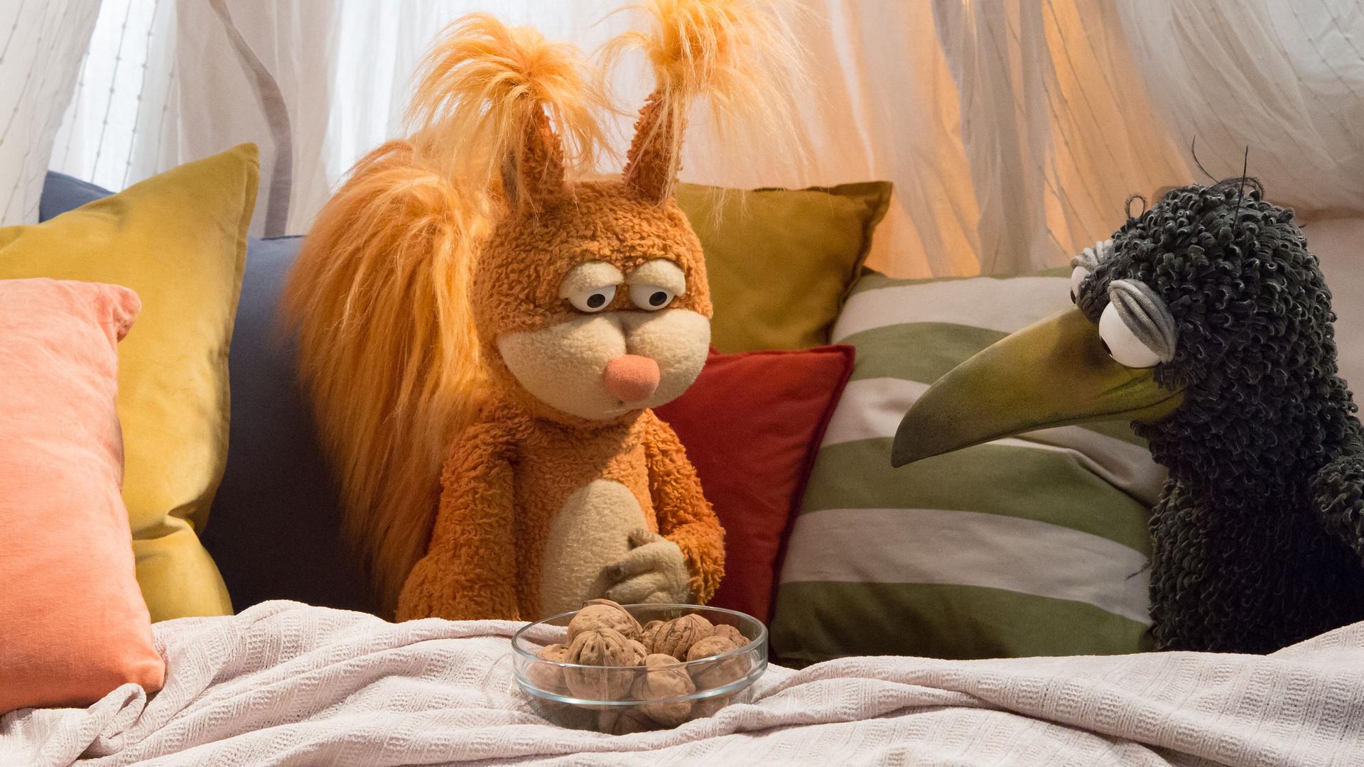 Rabe Rudi und Teddy sind in der gemütlichen Kuschelecke. Neben ihnen steht die Grammophon-Kiste, die ihnen eine Geschichte zeigen wird.