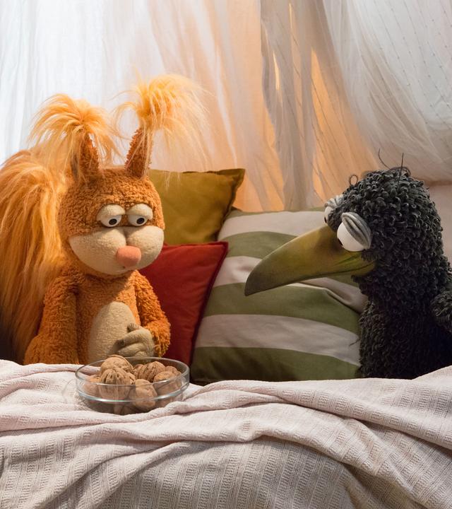 Rabe Rudi und Teddy sind in der gemütlichen Kuschelecke. Neben ihnen steht die Grammophon-Kiste, die ihnen eine Geschichte zeigen wird.