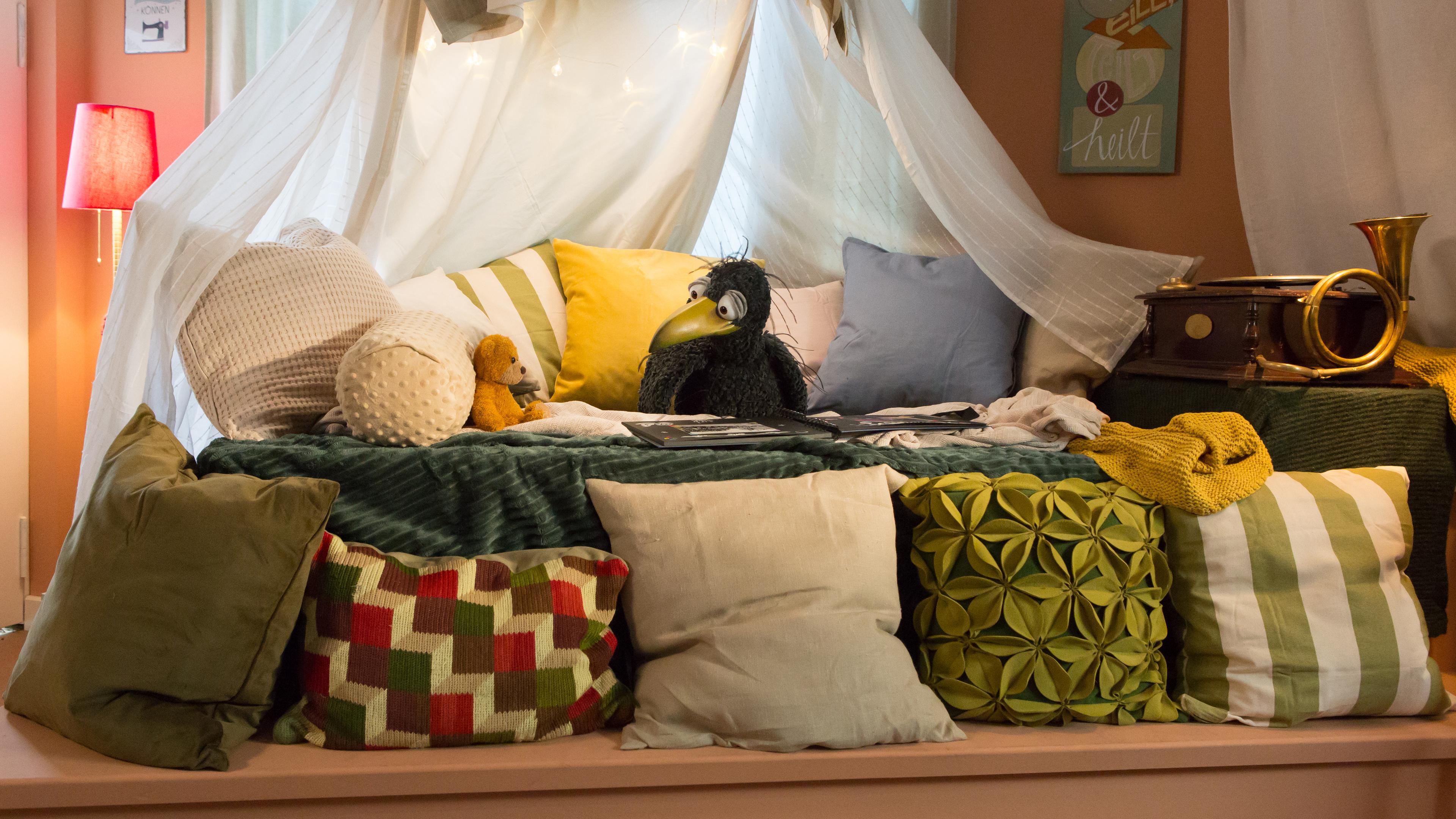 Rabe Rudi und Teddy sind in der gemütlichen Kuschelecke. Neben ihnen steht die Grammophon-Kiste, die ihnen eine Geschichte zeigen wird.