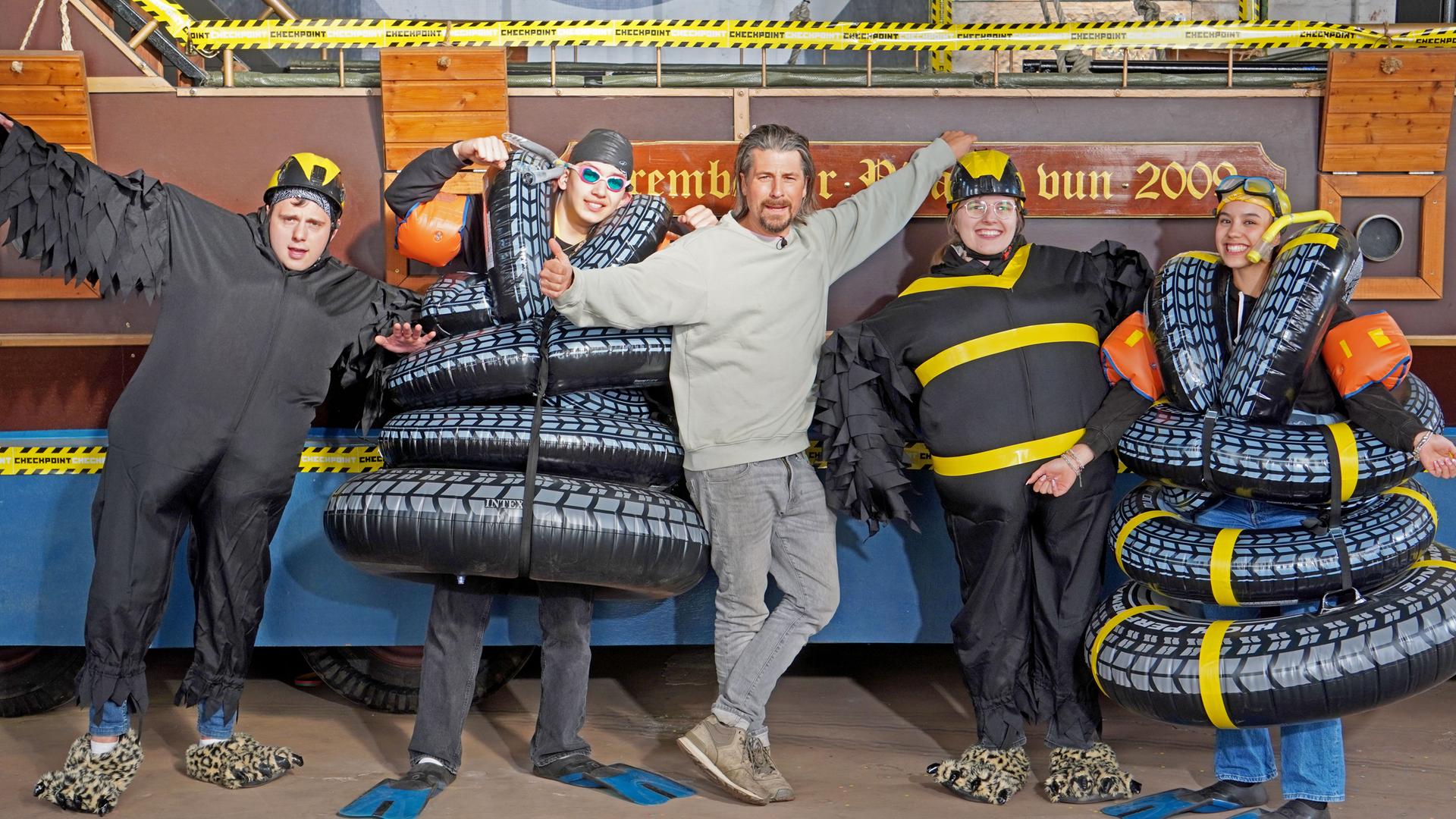 Checkpoint: Vier Mitglieder des Checkpoint-Teams stehen in selbstgemachten Kostümen gemeinsam mit Tommy Scheel in der Checkpoint-Halle. 