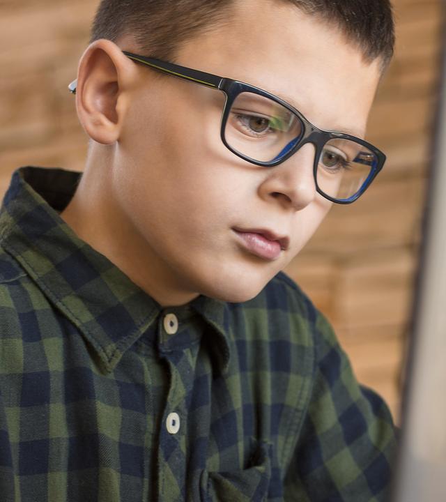 Ein Schüler blickt aufmerksam auf einen Monitor und ist in eine Arbeitsaufgabe vertieft. Die Darstellung vermittelt eine typische Lernsituation im Rahmen eines Praktikums.