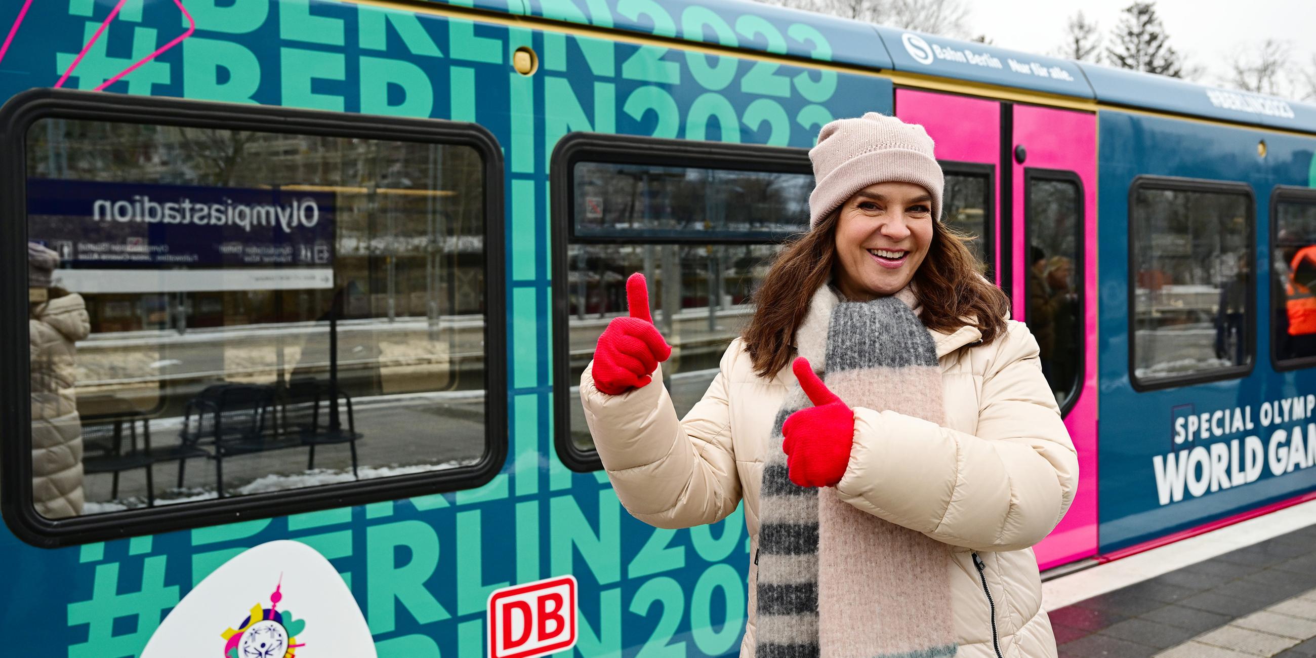 Katarina Witt, ehemalige Eiskunstläuferin, steht auf Bahnsteig 8 des Bahnhofs Olympiastadion vor einem im Design der Special Olympics World Games Berlin 2023 gestalteten S-Bahnzug.