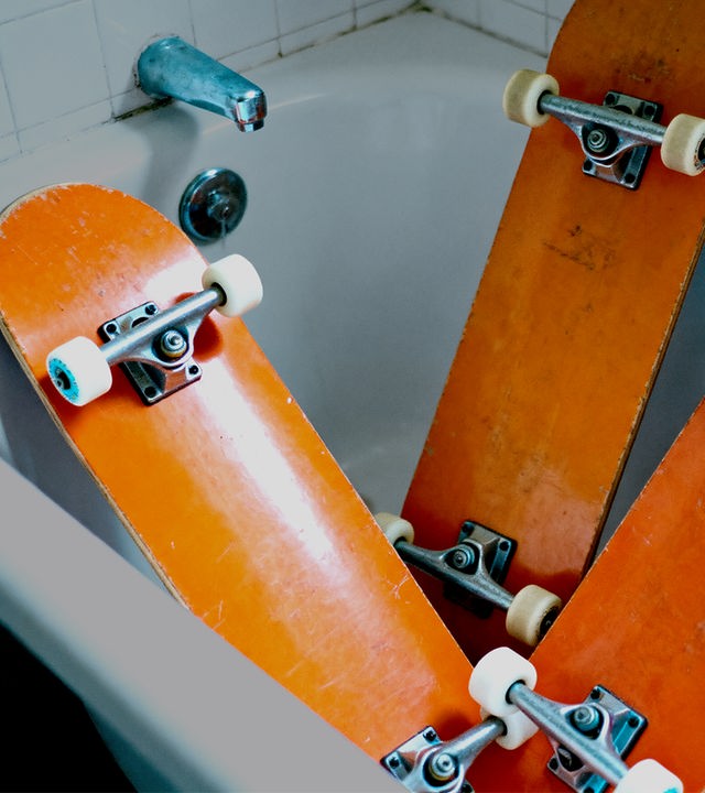 Auf dem Bild sind drei orangefarbige Skateboards zu sehen. Die Skateboards stehen mit der Unterseite zur Kammera gewand in einer leeren Badewanne.