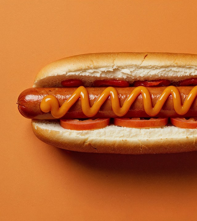 Auf dem Bild ist ein Hotdog vor orangenem Grund zu sehen. 