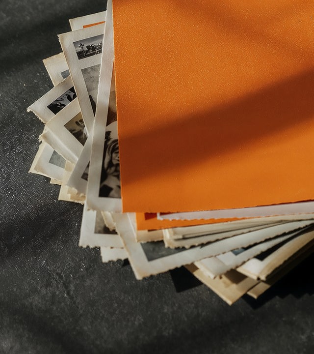Auf dem Bild ist ein Stapel alter Schwarzweiß-Fotos zu sehen. Ganz oben auf dem Stapel liegt ein komplett orangenes Foto.