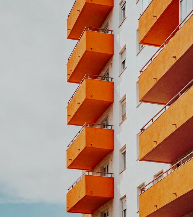 Auf dem Bild ist eine Hausfassade zu sehen. An der Hausfassade befinden sich sechs orangene Balkone.