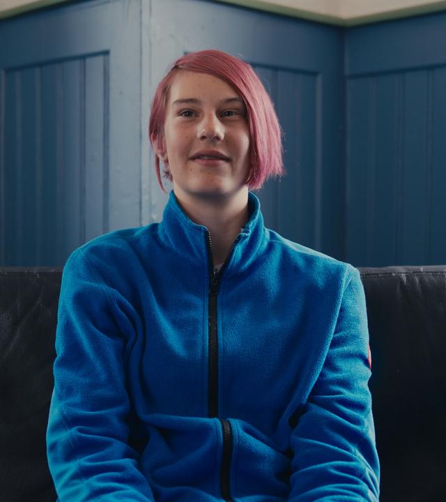 Marina sitzt auf einer Couch und lächelt in die Kamera. 