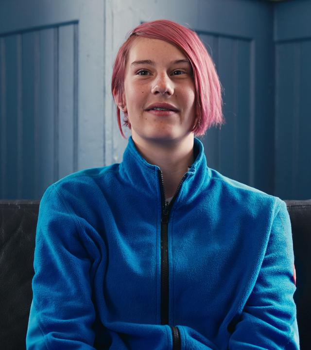 Marina sitzt auf einer Couch und lächelt in die Kamera. 