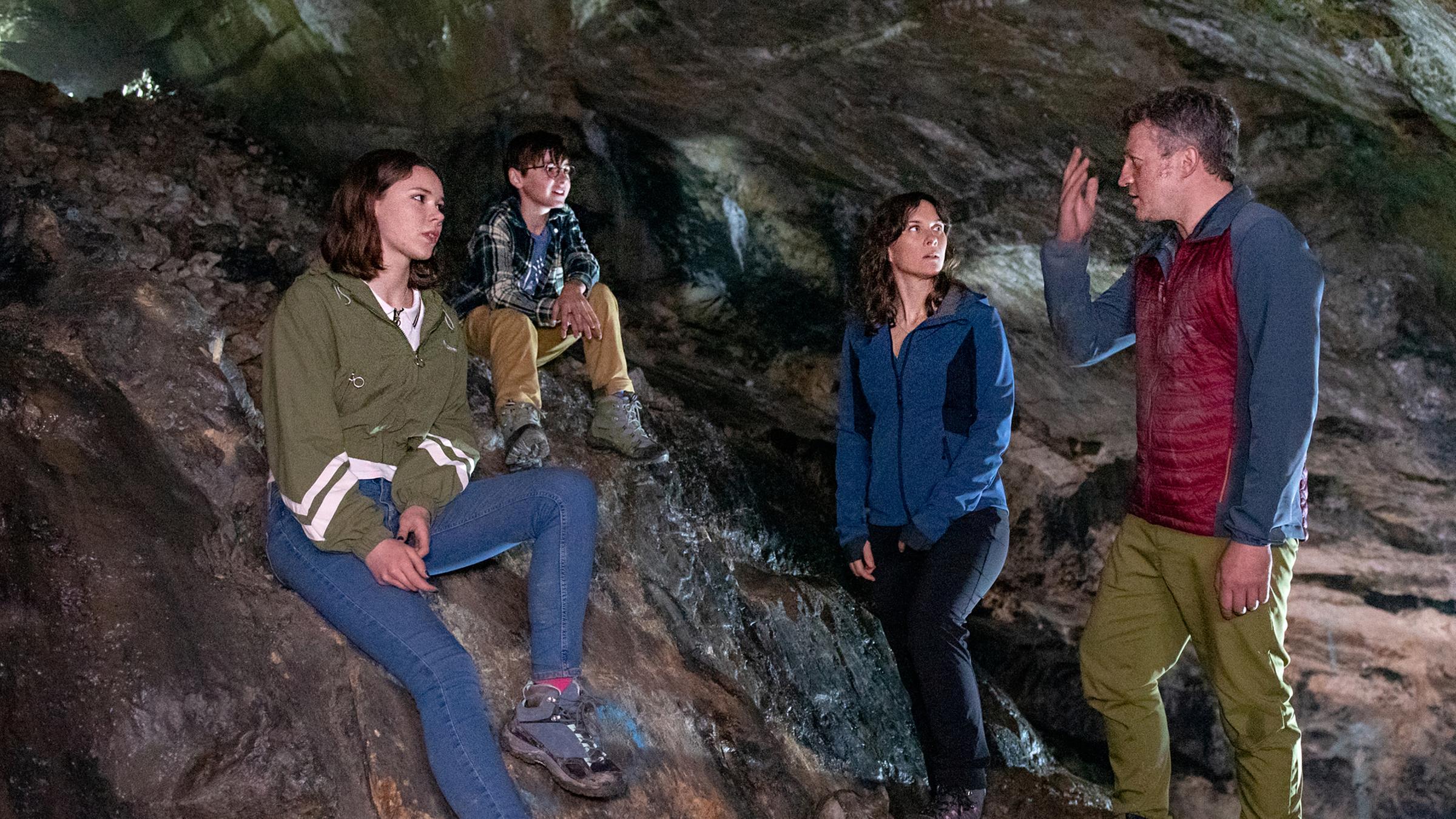 Vier Personen in einer Höhle: Die beiden Kinder Emma (Moana Marie Goetze) und Linus (Timo Hack) sitzen auf Felsgestein, Cathrin (Kathrin von Steinburg) und Frank (Josef Heynert) stehen.