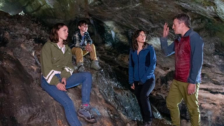 Vier Personen in einer Höhle: Die beiden Kinder Emma (Moana Marie Goetze) und Linus (Timo Hack) sitzen auf Felsgestein, Cathrin (Kathrin von Steinburg) und Frank (Josef Heynert) stehen.