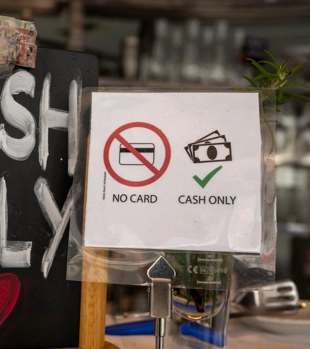 Ein Schild mit der Aufschrift «No Card - Cash Only» (Keine Karte - nur Bargeld) steht in einem Café in der Innenstadt auf einem Tresen.