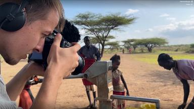 Nahaufnahme: ZDF-Kameramann filmt an einem Brunnen, an dem eine kenianische Nomadin Wasser entnimmt.