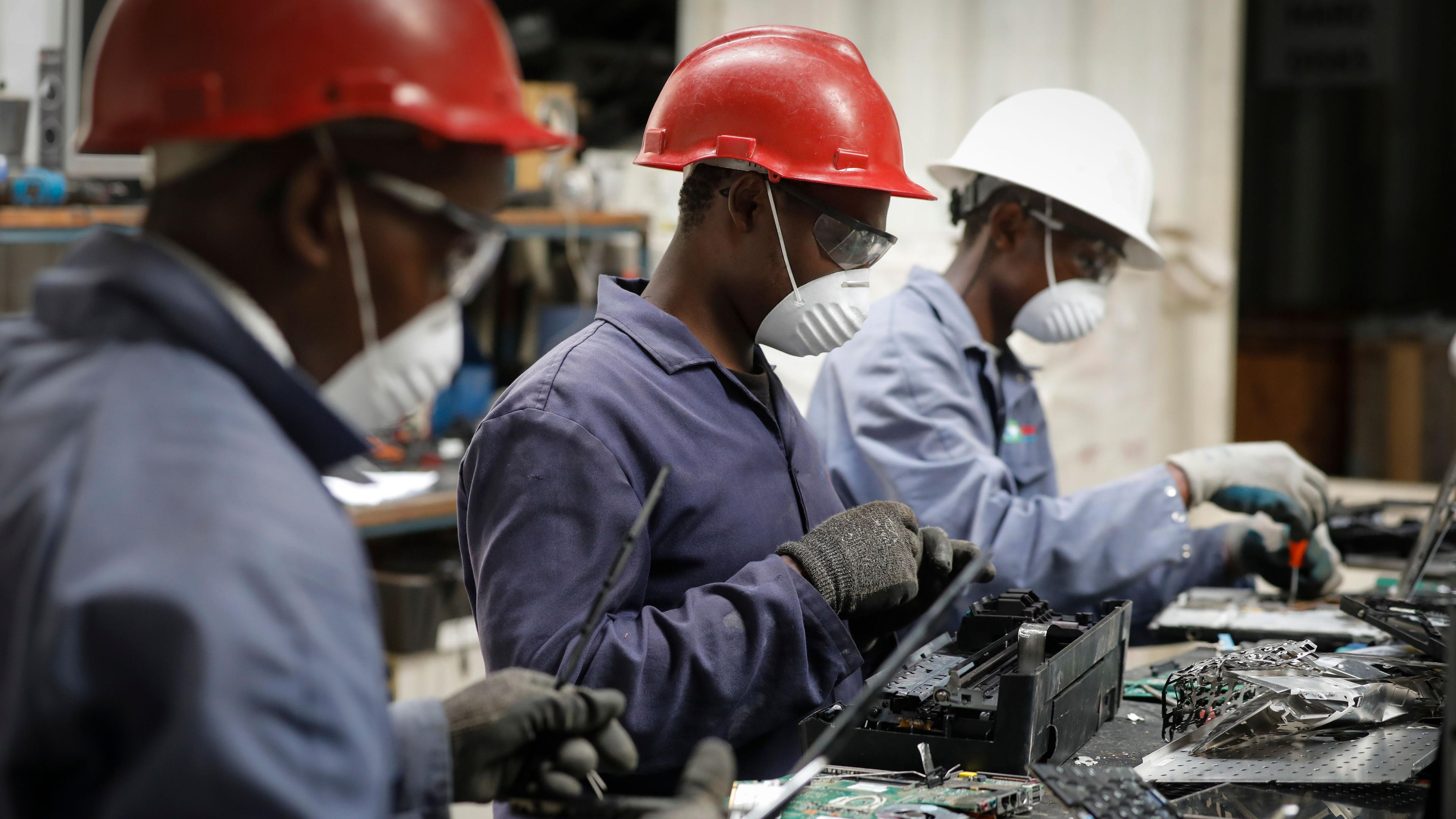 Afrikanische Facharbeiter in einer Fabrik mit Atemschutzmasken und Helmen. 