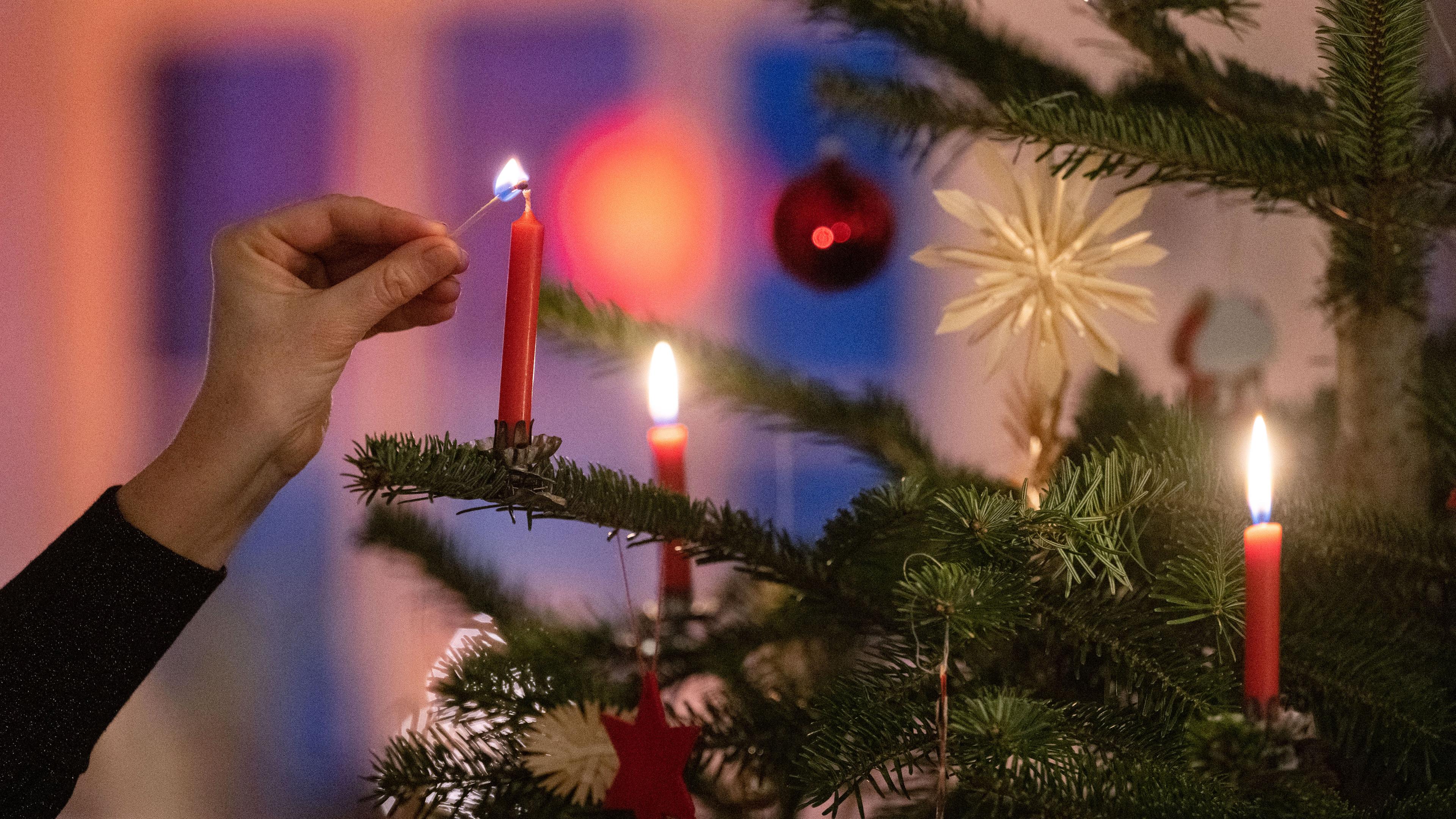 Eine Kerze wird an einem geschmücktem Weihnachtsbaum angezündet.
