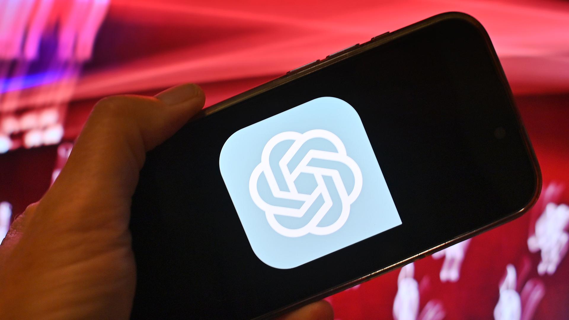 Hand zeigt ein Smartphone mit dem ChatGPT Logo vor rotem Hintergrund