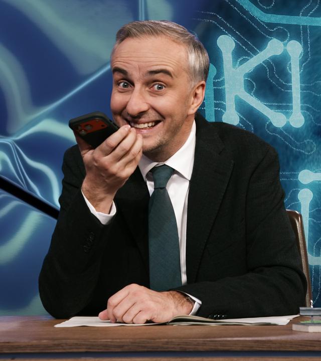 Jan Böhmermann sitzt am Schreibtisch und spricht in sein Smartphone. Rechts von ihm im Hintergrund steht "KI CHAT BOTS", hinter dem Schriftzug ist schemenhaft ein künstlich gestaltetes Gesicht abgebildet.