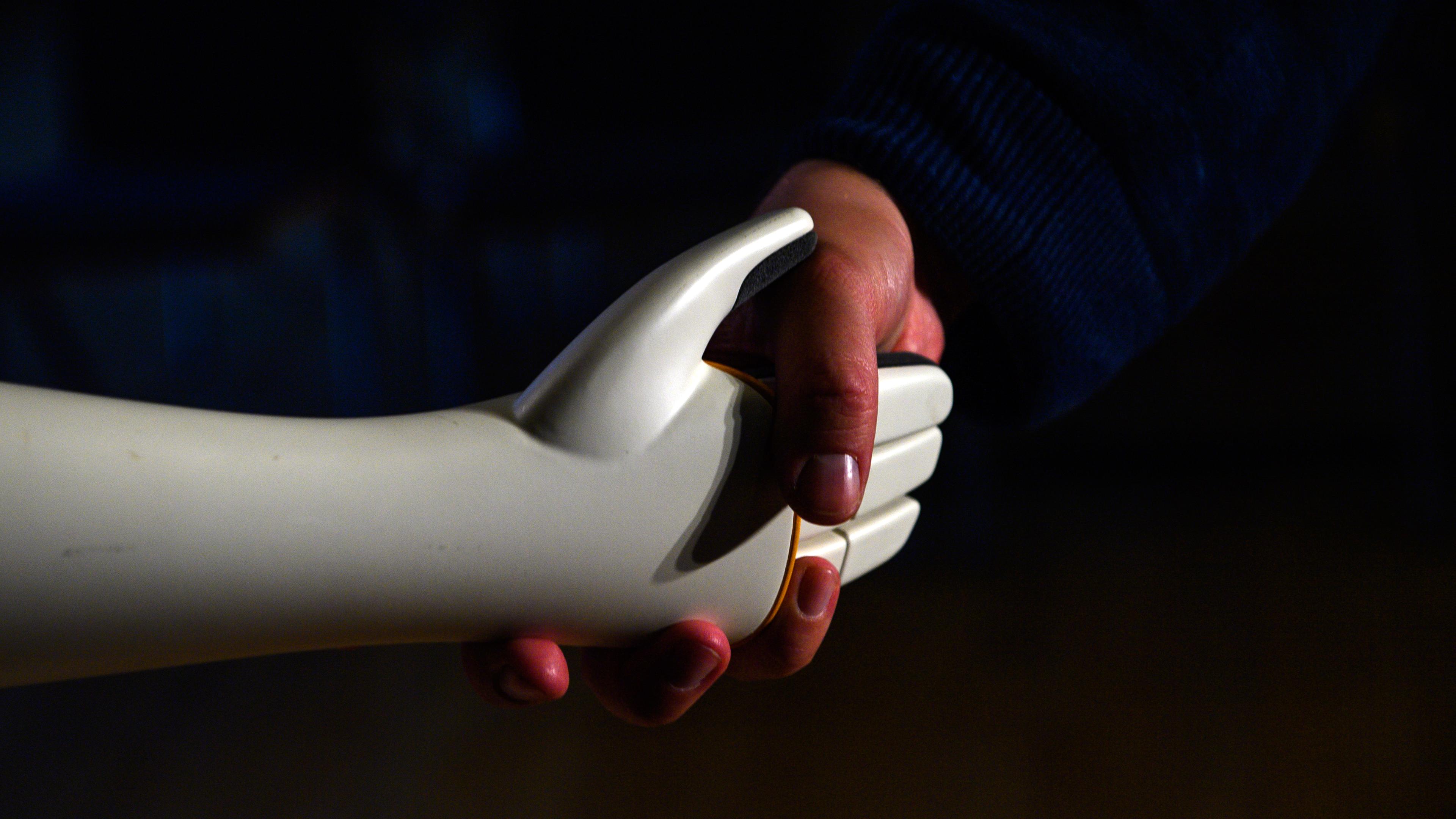 Eine Person reicht dem humanoiden Roboter "Ari" die Hände.