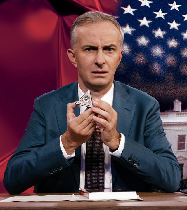 Jan Böhmermann sitzt am Schreibtisch und hält ein sogenanntes "Auge der Vorsehung" in den Händen. Im Hintergrund sind das Weiße Haus und die Flagge der USA abgebildet.