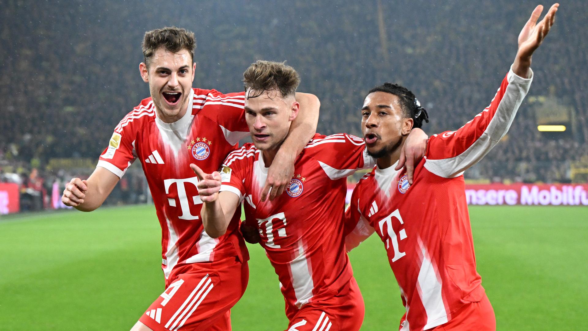 Bayerns Mittelfeldspieler Joshua Kimmich jubelt zusammen mit seinen Teamkollegen Josip Stanisic und Michael Olise nach seinem Tor zum 2:3 Endstand gegen den BVB