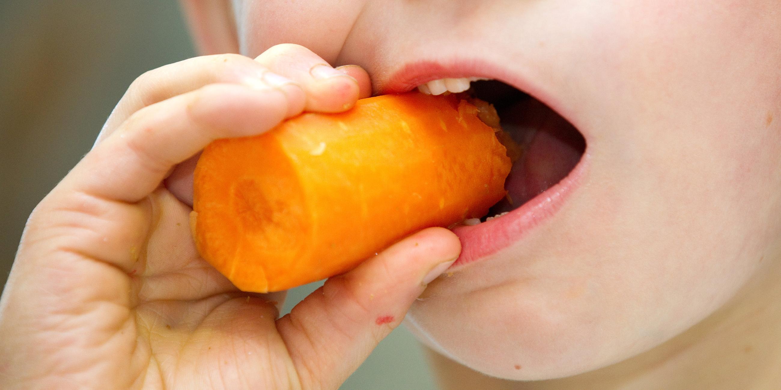 Kind beißt in eine Karotte