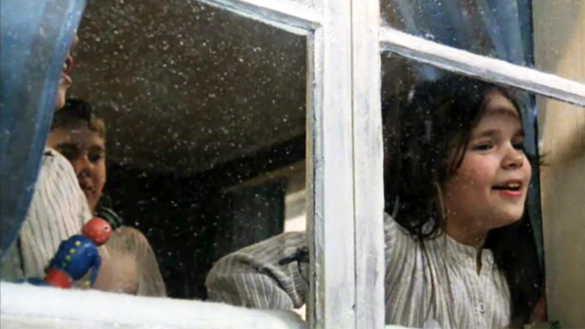 Die Kinder sind aufgewacht, schauen aus dem Fenster und sehen den ersten Schnee fallen.