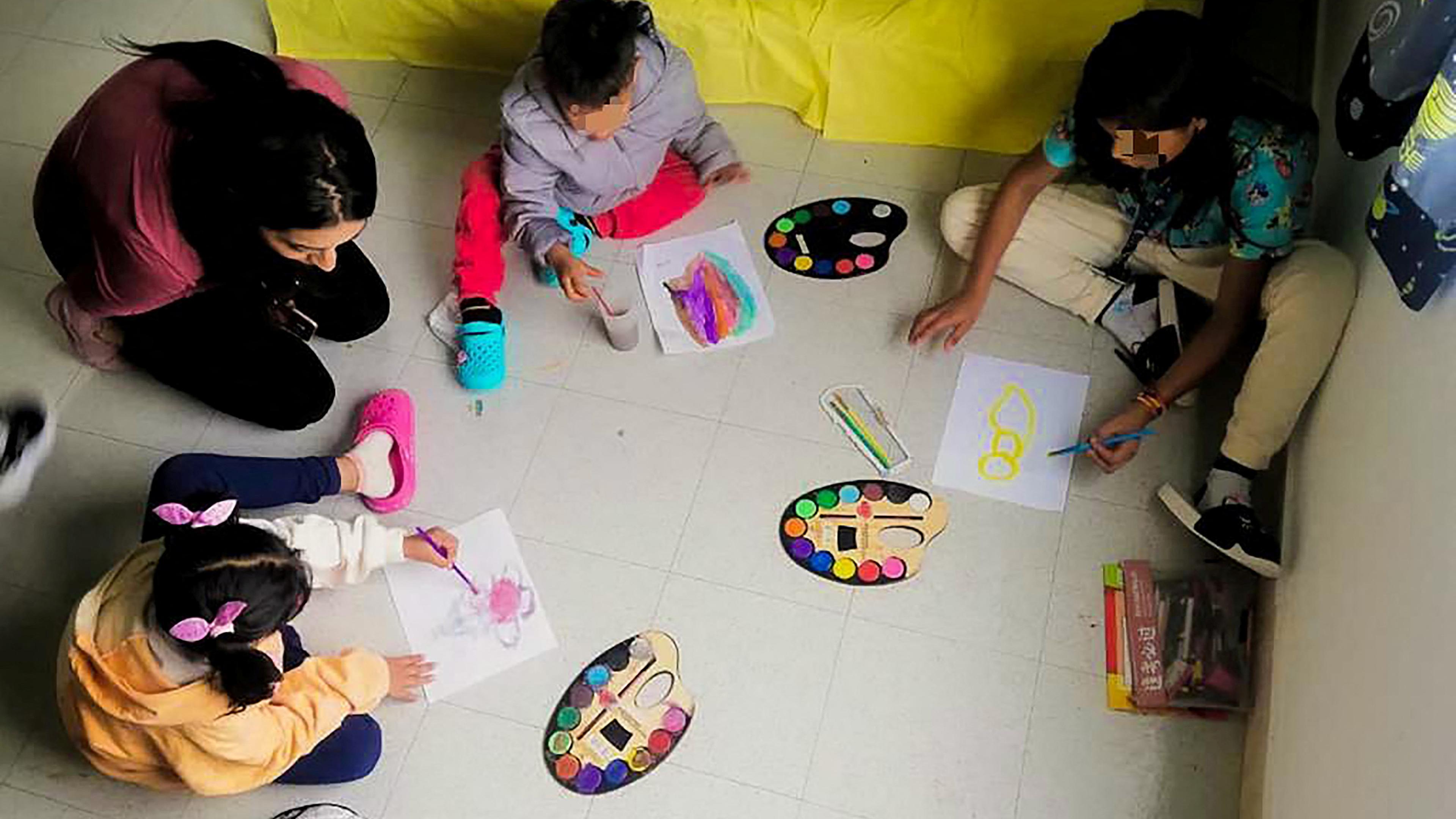Drei der Kinder, die wochenlang alleine im kolumbianischen Dschungel lebten, sitzen mit einer Betreuerin am Boden und malen.