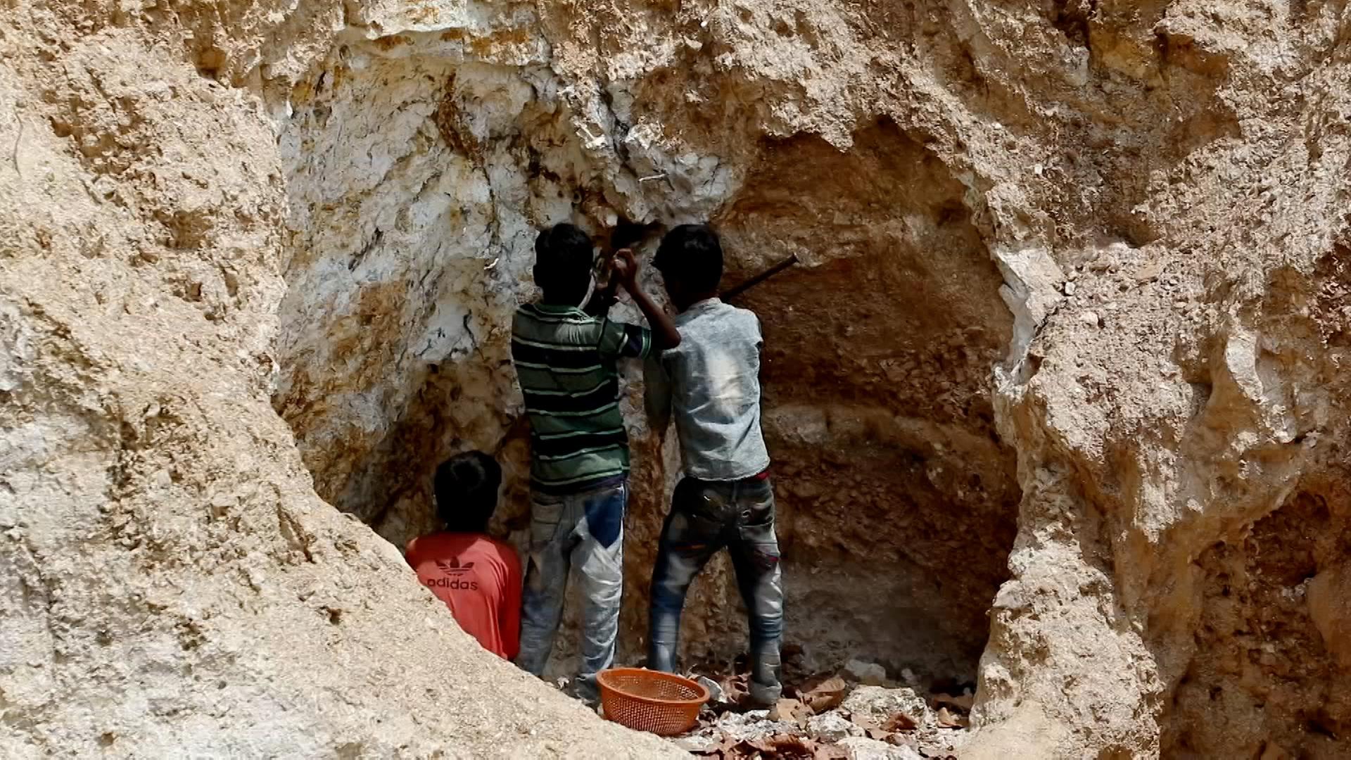 Auf dem Bild sind drei Kinder zu sehen, die Mica-Mineralien in einer Grube abbauen.