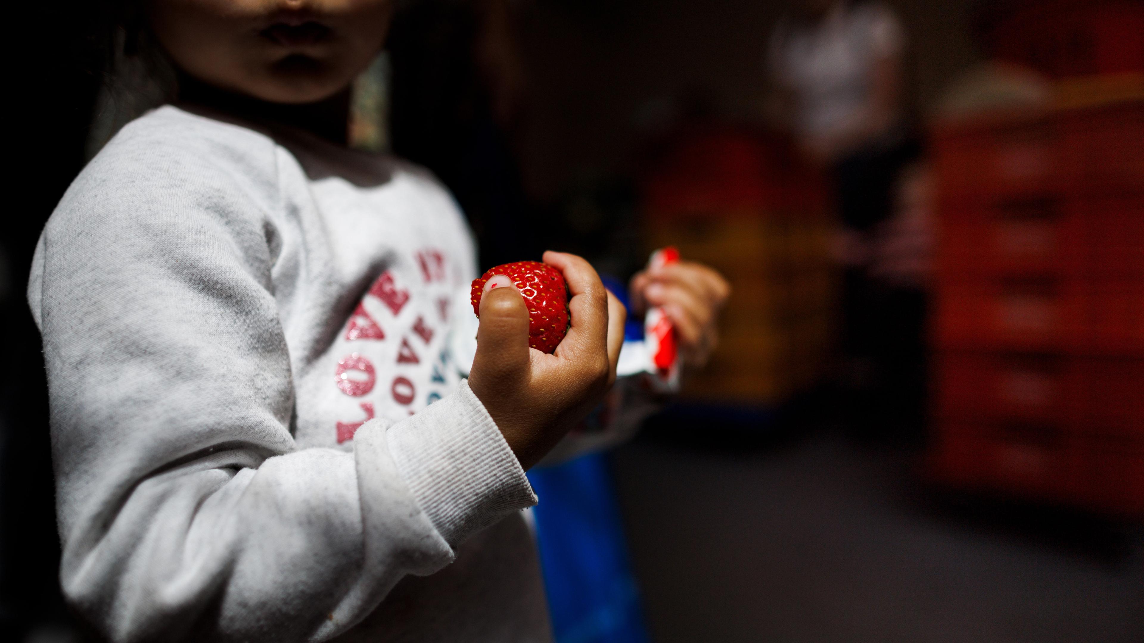 Ein kleines Kind hält eine Erdbeere und Schokolade in den Händen in der Ausgabestelle Paul-Schneider-Haus der Berliner Tafel. 