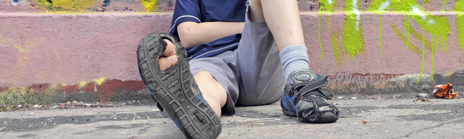 Junge mit kaputtem Schuh sitzt auf einer Strasse