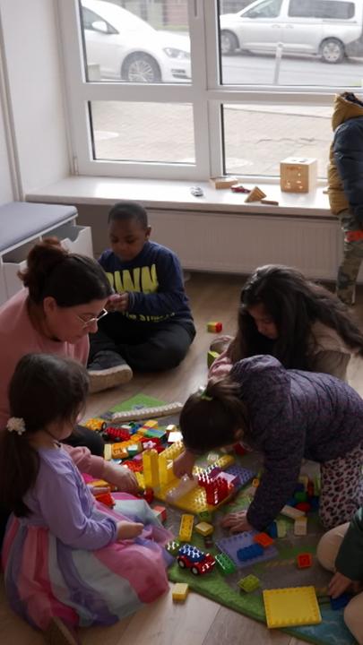 Eine Erzieherin spielt mit Kindern Lego.