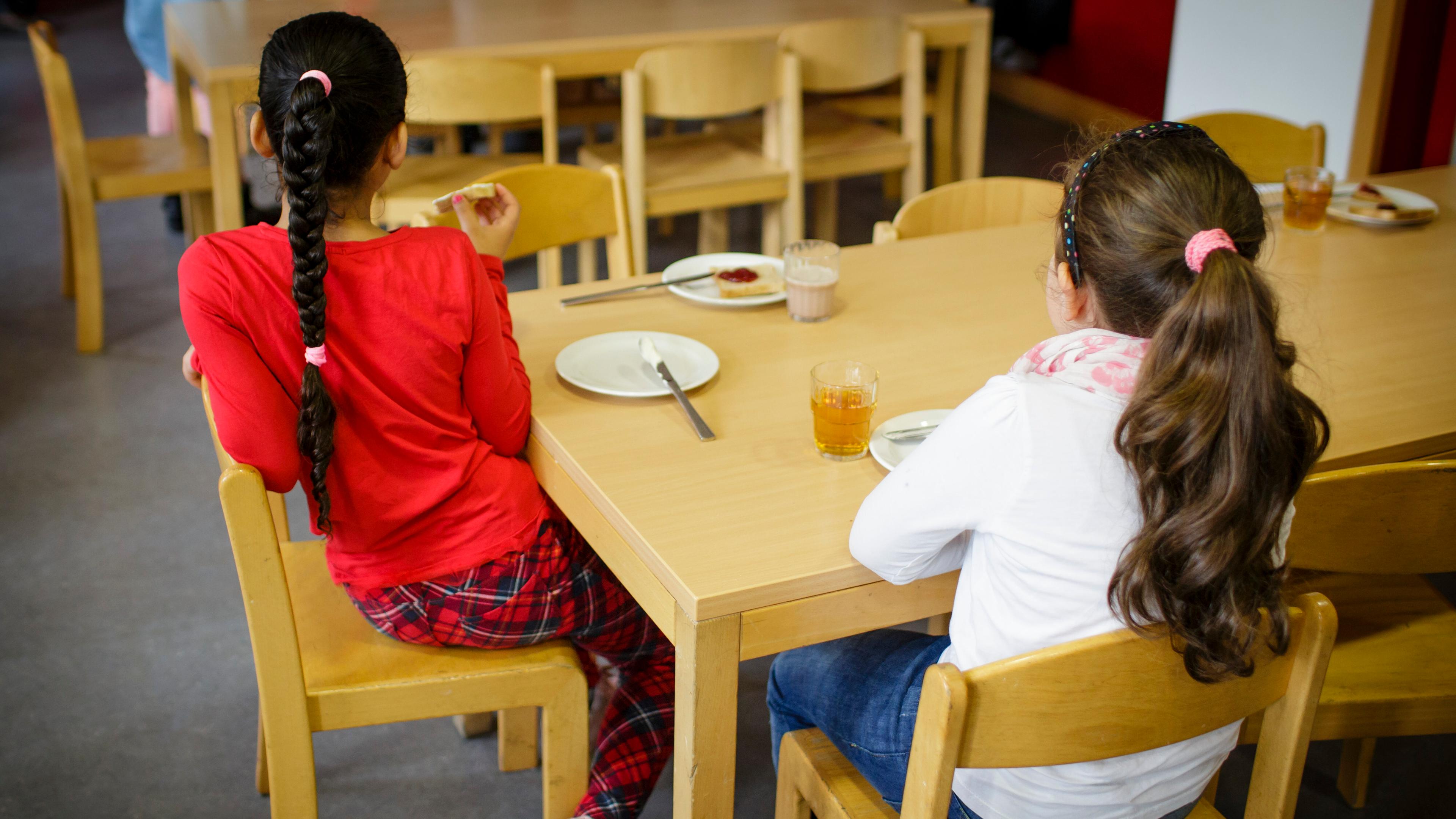 Kinder sitzen zum Frühstück in einer Grundschule an einem Tisch.