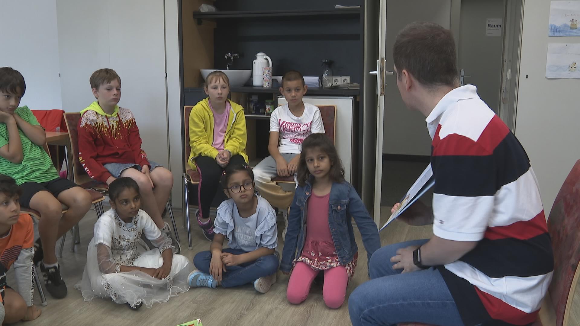Kinder sitzen im Kreis mit Deutschlehrer in Raum der Volkshochschule Bingen