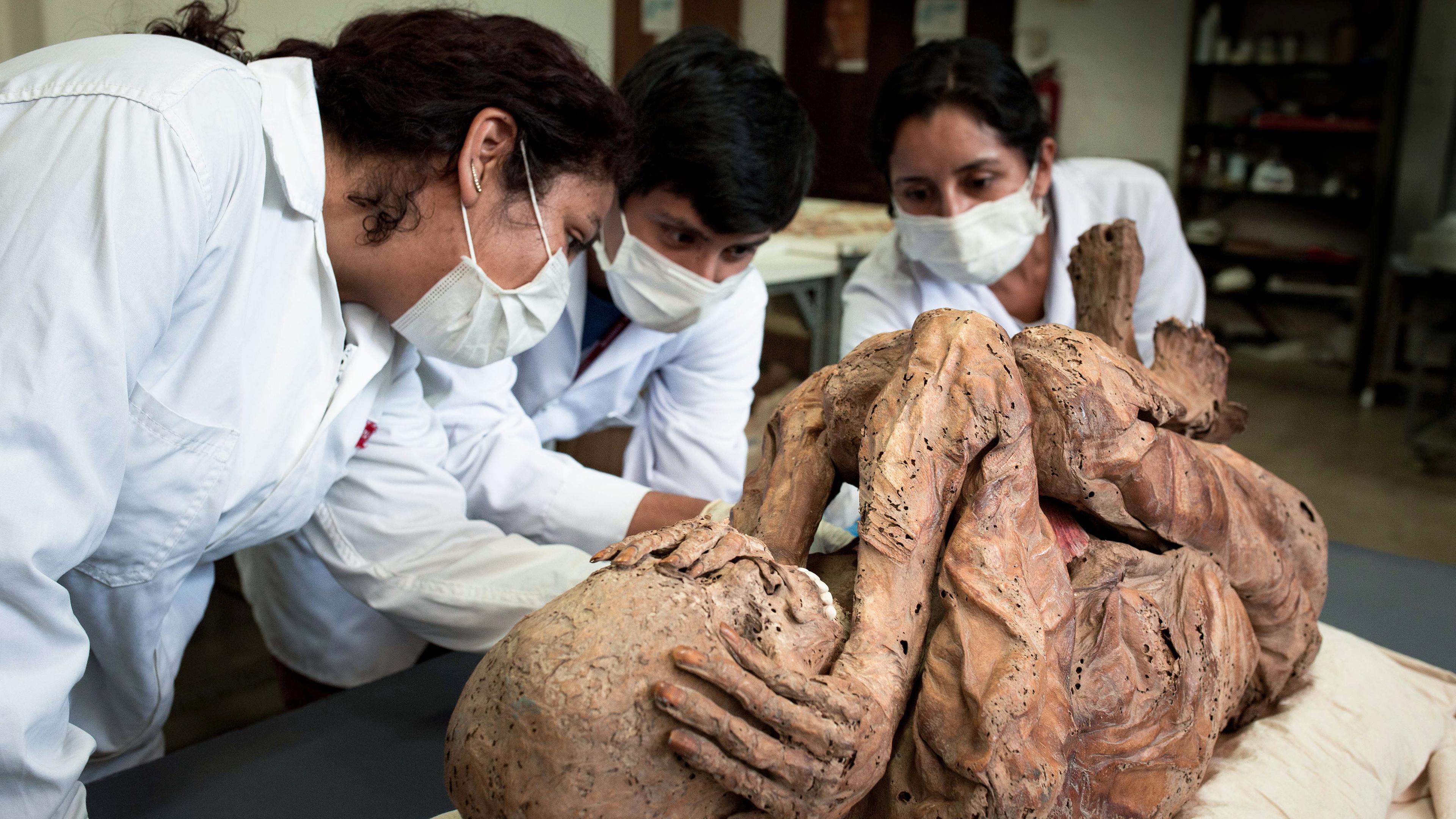 Eine Kindermumie in Lima, davor Forscher studierend.