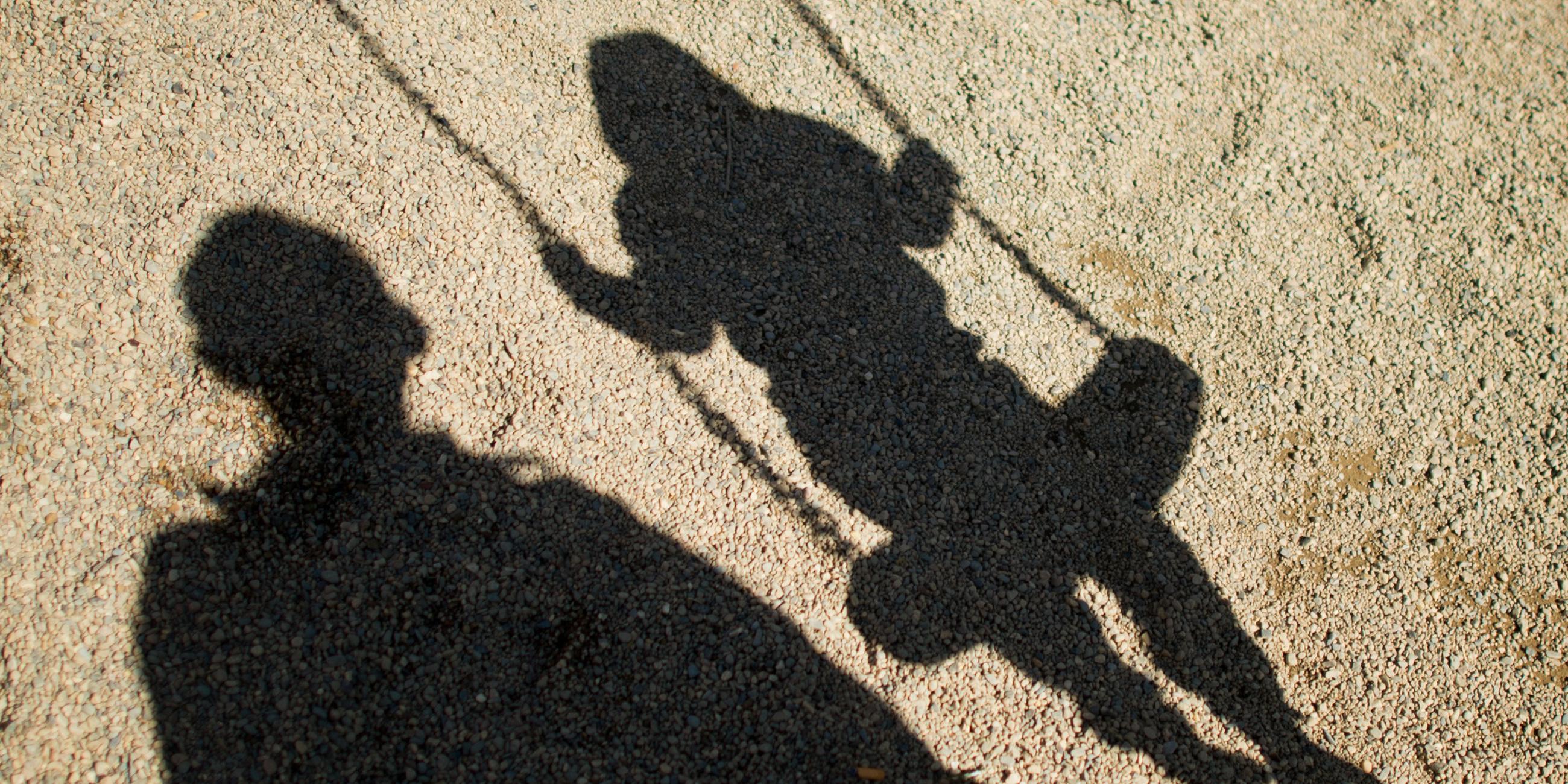 Schatten eines Kindes auf einer Schaukel und eines Erwachsenen daneben