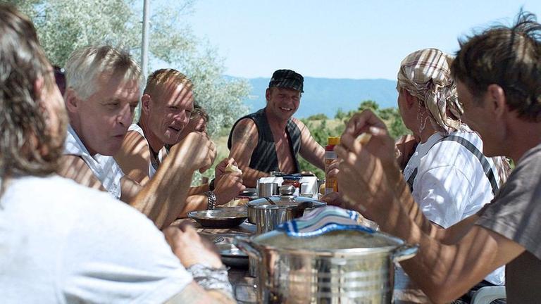 "Western": Eine Gruppe Männer sitzt im Freien zum Mittagessen um einen Tisch herum