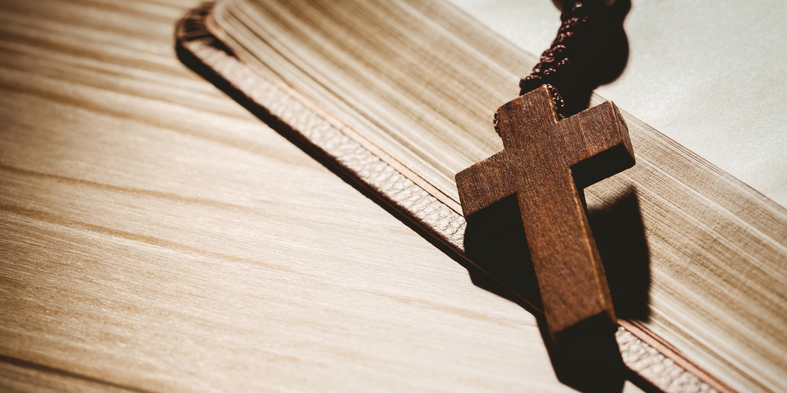 Ein Kreuz aus Holz liegt auf einer aufgeschlagenen Bibel